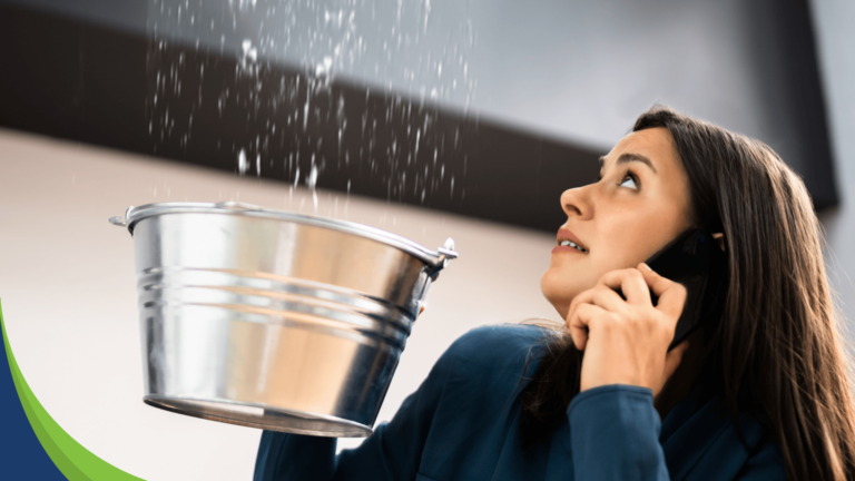 Woman uses bucket to catch water leak while using phone to call restoration company